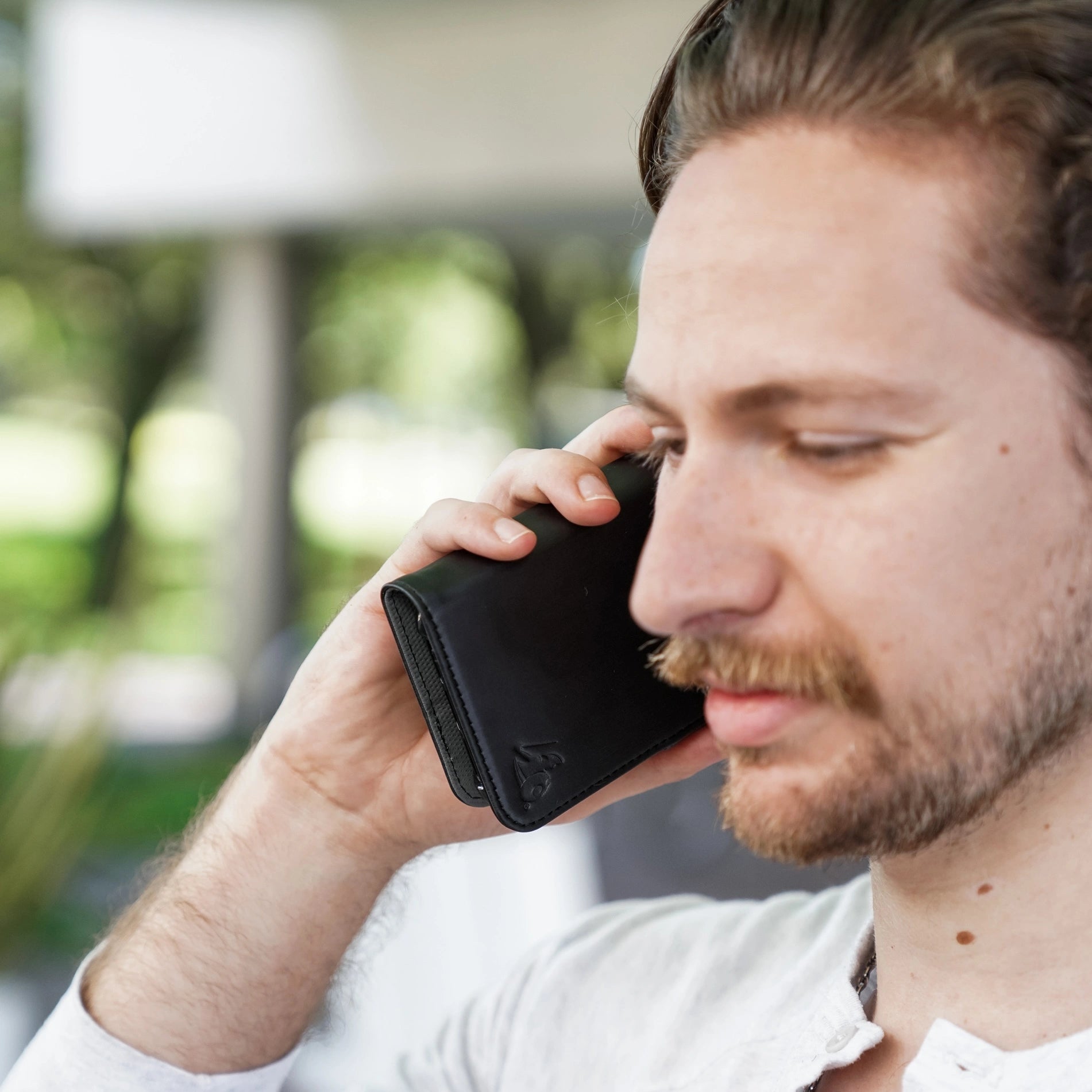 DefenderShield EMF Protection iPhone 17 Wallet Case Man Holding Black Phone Outside