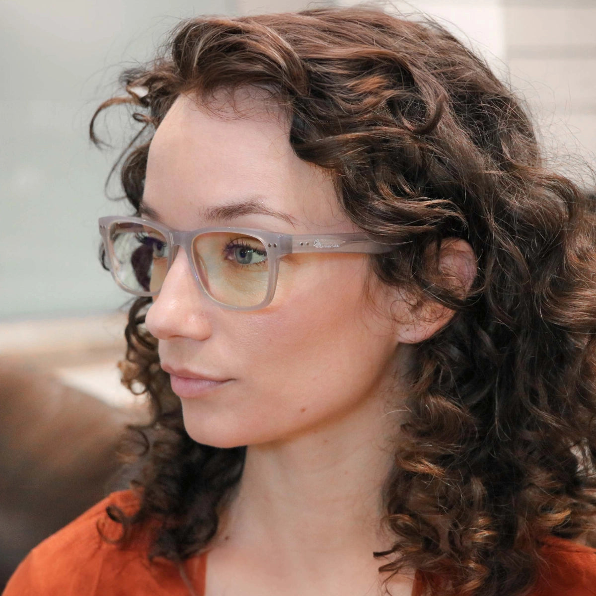 Woman with curly hair wearing Signature Blue Light Glasses and an orange top