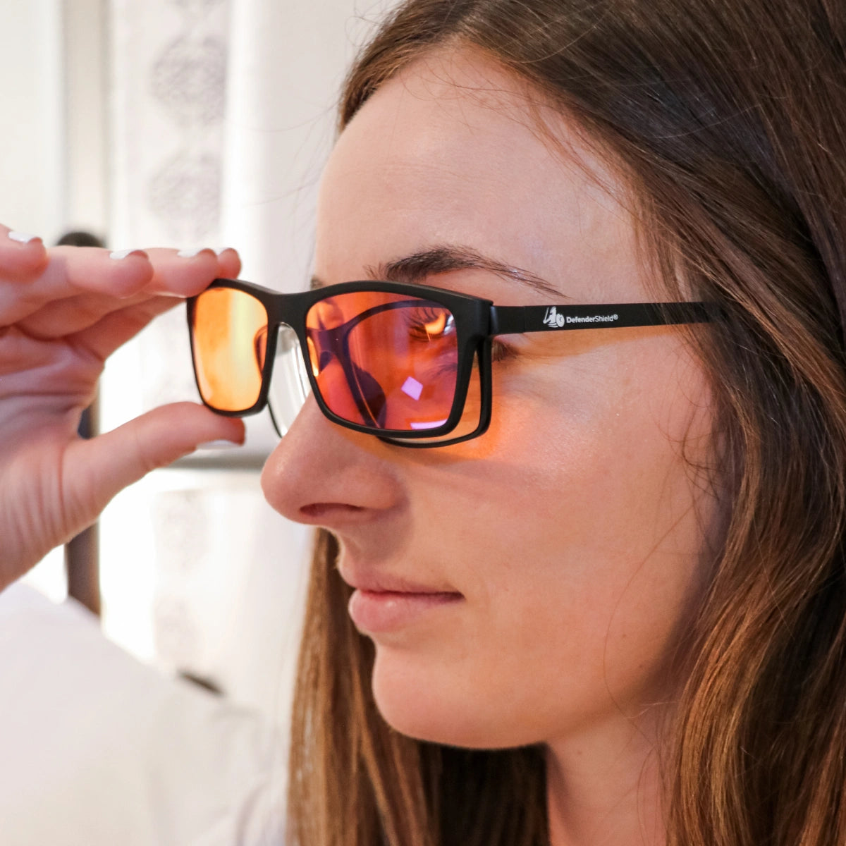 Person holding a pair of sunglasses with orange-tinted lenses and black frame.